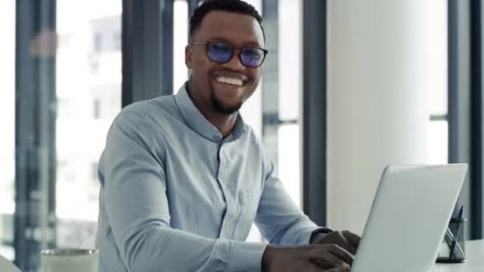 一个快乐而自信的年轻非洲裔美国商人在现代办公室里使用笔记本电脑。一个微笑的商人在桌子上的电脑上工作的