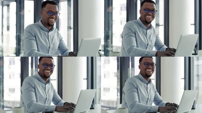 一个快乐而自信的年轻非洲裔美国商人在现代办公室里使用笔记本电脑。一个微笑的商人在桌子上的电脑上工作的