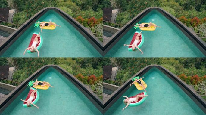 两个女人漂浮在游泳池里躺在充气玩具上最好的朋友暑假在热带酒店度假时玩得开心，穿着比基尼顶视图