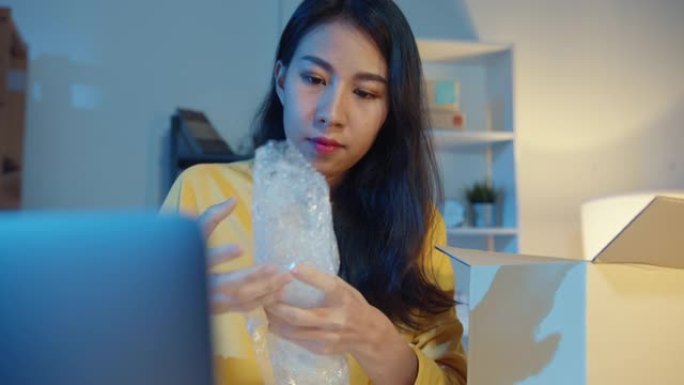 年轻的亚洲女商人包装玻璃使用气泡包装，晚上在家庭办公室支持损坏易碎产品。