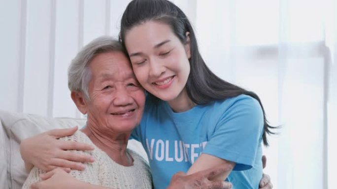 肖像亚洲年轻女性志愿者拥抱亚洲老年女性微笑着看着家里的镜头。志愿服务