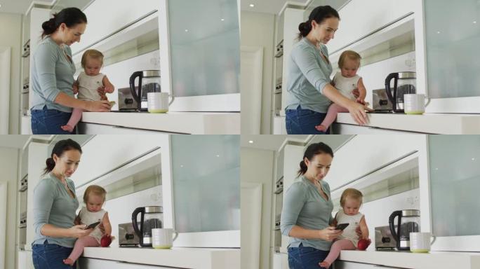 白人母亲在家里的厨房里用智能手机抱着婴儿
