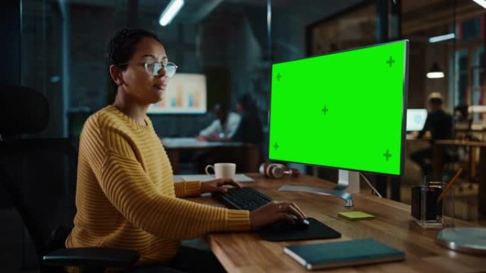 年轻的多民族专家在创意办公室的台式电脑上工作，绿屏模拟显示。美丽多样的短发和眼镜女经理穿着黄色套头衫