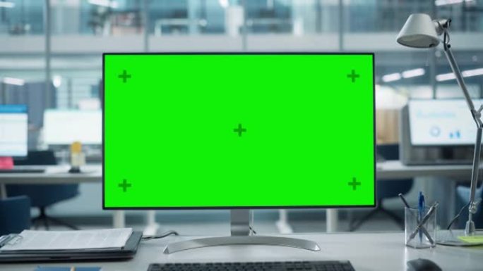台式电脑显示器，带有模拟绿屏色度键显示屏，站在现代商务办公室的桌子上。在带有大城市办公室的背景玻璃墙