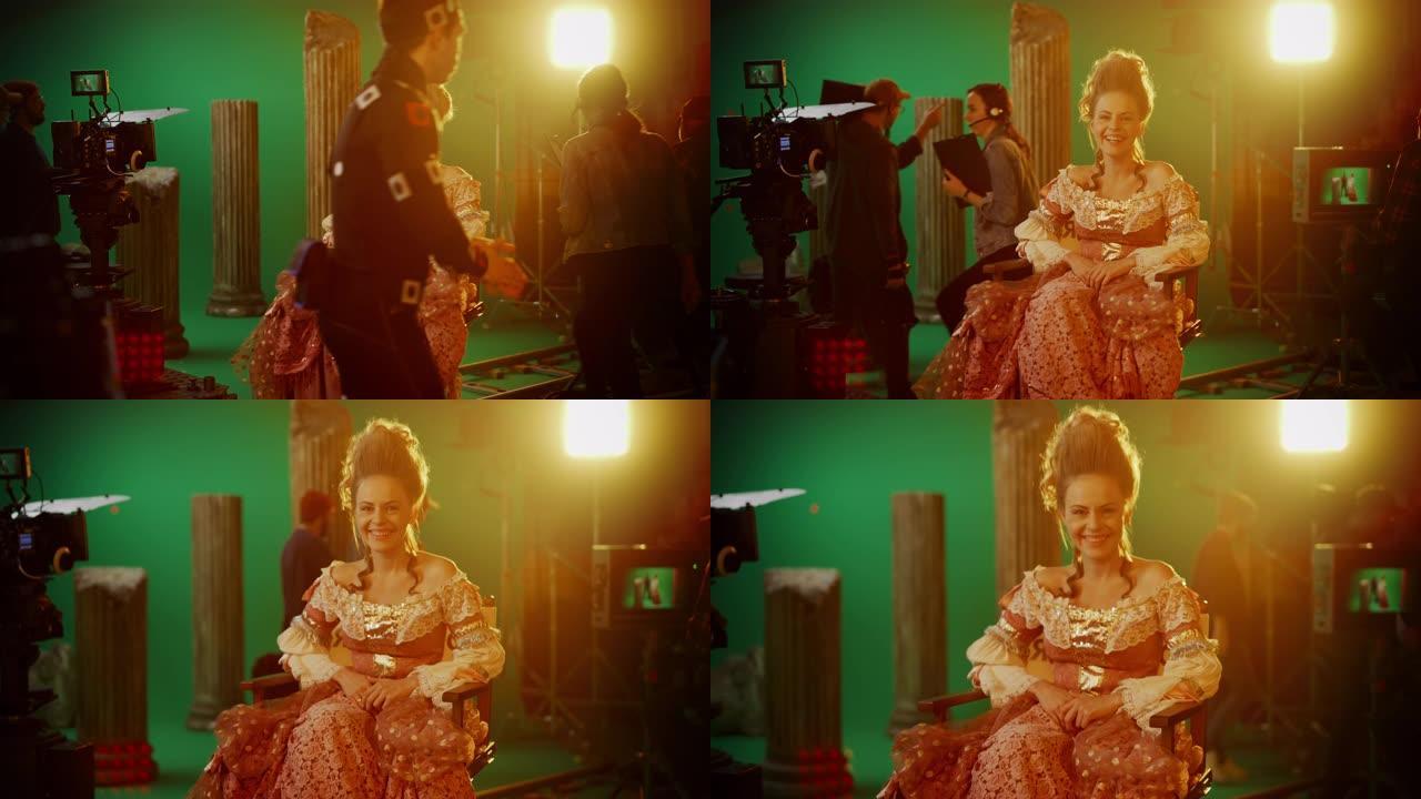 在古装戏剧电影中: 美丽的微笑女演员穿着文艺复兴时期的连衣裙，快乐地坐在椅子上，背景是绿色的屏幕。工