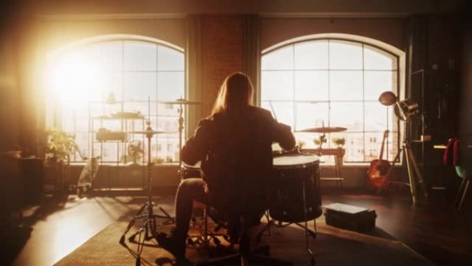 一个人背对着镜头坐着，在阳光下的阁楼工作室里进行乐队排练时打鼓。鼓手在舞台上的音乐会前独自练习。暖色