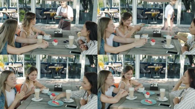 快乐的女性朋友在户外咖啡馆享用午餐，而女服务员在夏日带甜点