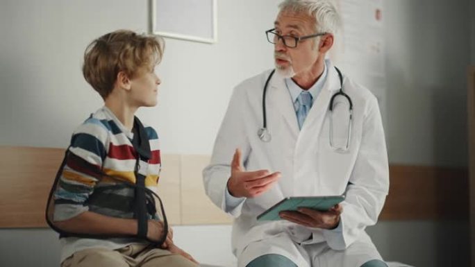友好的中年家庭医生与一个小男孩与手臂支撑和显示测试结果的平板电脑。快乐的医疗保健医生在医院安抚男孩断