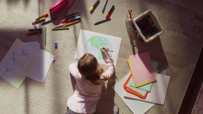 俯视图: 小女孩画我们美丽的地球。非常有才华的孩子在家里玩得开心，想象我们的家乡星球是一个快乐的地方