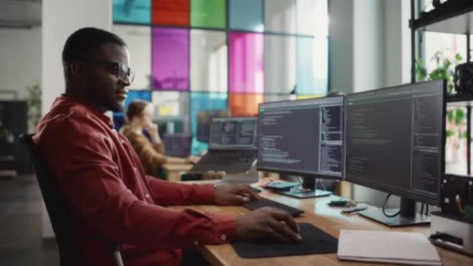 非裔美国人在台式计算机上编码，在创意办公室设置专业的多显示器。男软件工程师为创新型初创公司开发移动应