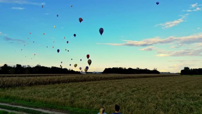 夫妇坐在面包车上，看着热气球在乡村天空中飞行