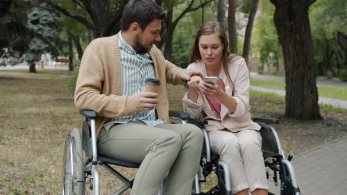 轮椅上的残疾夫妇使用智能手机喝酒去喝咖啡和在户外聊天