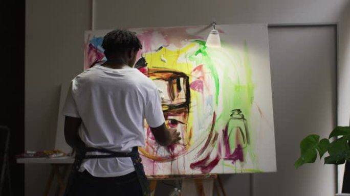 非裔美国男性艺术家在艺术工作室的画布上穿着围裙绘画的后视图