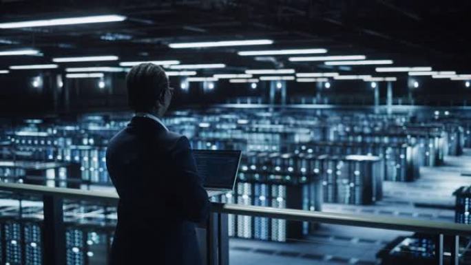 女性IT专家在数据中心使用笔记本电脑，走在俯瞰大服务器场云计算设施的桥上。女商人，电子商务企业家。基