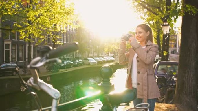快乐的游客探索阿姆斯特丹，站在运河旁边，在日落时用智能手机拍照