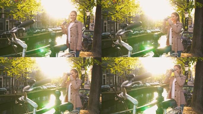 快乐的游客探索阿姆斯特丹，站在运河旁边，在日落时用智能手机拍照