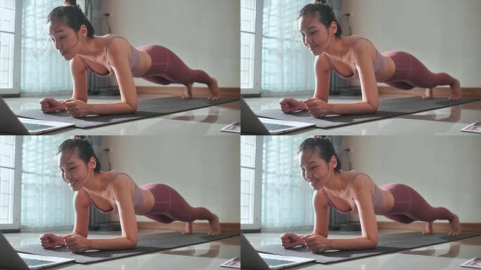 年轻女子在公寓里用笔记本电脑在垫子上做瑜伽观看教程