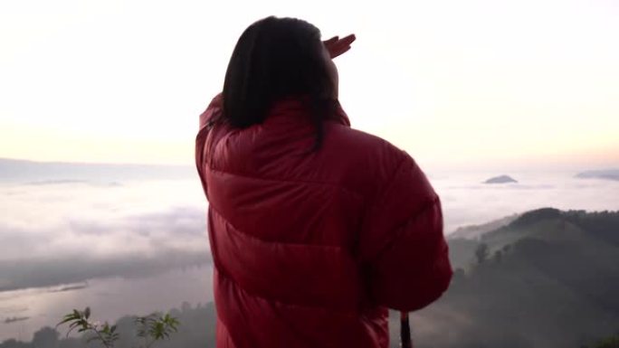剪影年轻女子看着山上的风景，带着阳光和雾。独自旅行背包客带着相机徒步旅行。假日旅行和度假概念。