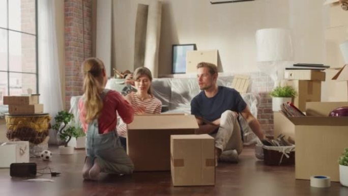 快乐的房主搬进来: 可爱的夫妇坐在舒适公寓的地板上打开纸板箱，小女儿加入了他们的行列。欢快的一天，和