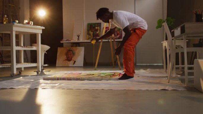 非裔美国男艺术家在画布上倒油漆，并在艺术工作室绘画