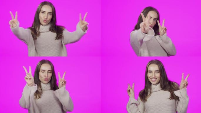4k视频片段，一位迷人的年轻女子在粉红色的工作室背景下做出和平姿态