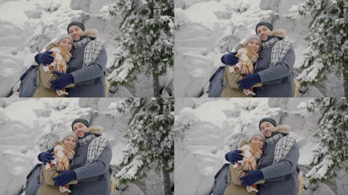 站在冬季森林里的快乐年轻夫妇的慢动作肖像，微笑着看着相机