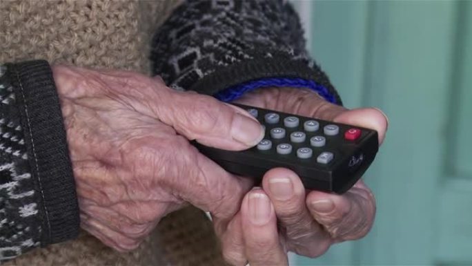 一个拿着电视遥控器的老妇人皱巴巴的手在家里。特写。4k分辨率。