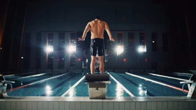 肌肉发达的男性游泳者来到起跑器跳进游泳池。职业男子运动员准备赢得冠军。电影光，慢动作，耀斑光，后视图