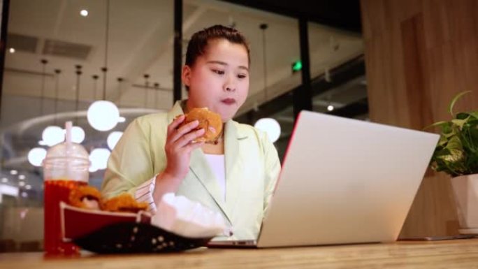 女商人在使用笔记本电脑时吃快餐
