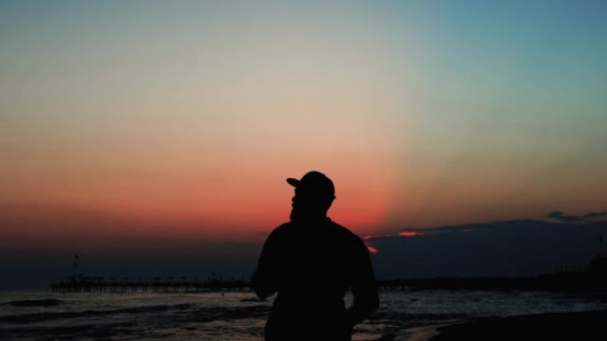快乐旅游男人的史诗般的电影剪影，带着相机在海边享受令人惊叹的红霞，向前走。
