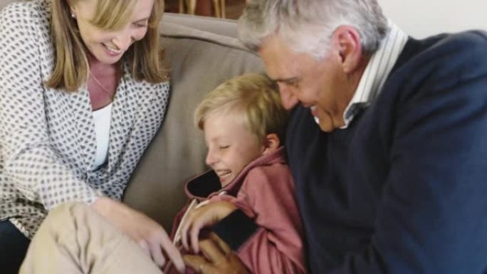 家庭在家里玩得开心。一个高级男人和女人在挠他们的小男孩。爷爷奶奶和可爱的孙子在沙发上玩耍