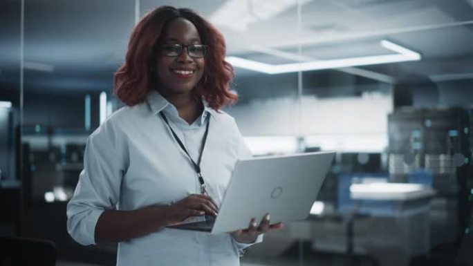 一位戴着眼镜，使用笔记本电脑，看着相机并微笑着的黑人女性的肖像。非洲信息技术专家、软件工程师或开发者