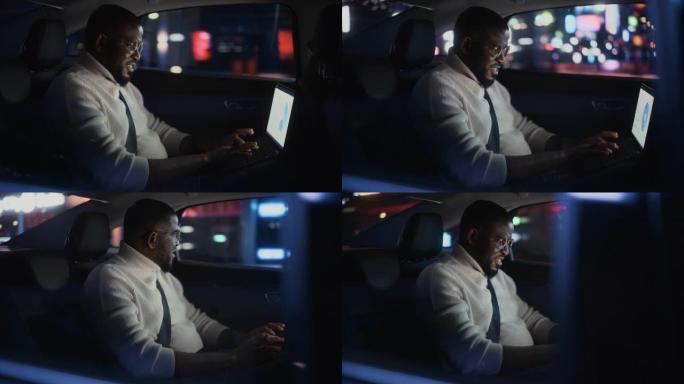时髦的戴眼镜的黑人在晚上坐出租车的后座上下班。男性使用笔记本电脑，在城市街道上开着霓虹灯的汽车时看着