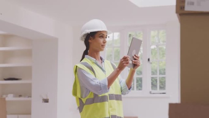 戴着带数字平板电脑的安全帽的女建筑商拍照并检查物业内新厨房单元的交付-慢动作拍摄
