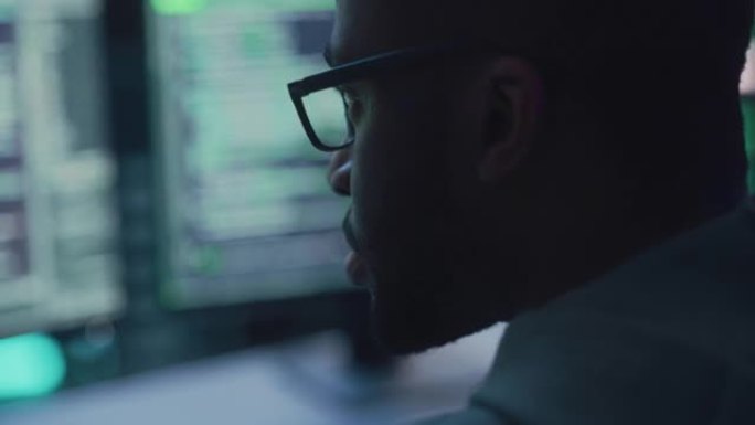 特写黑人男性程序员看着台式电脑显示器的肖像。专业开发人员编写代码，从事高科技项目。编码和发展工作概念