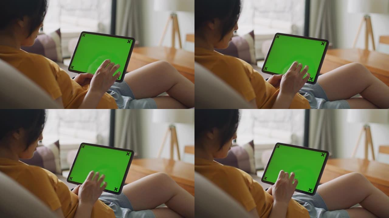 年轻女子在沙发上使用绿屏数字平板电脑