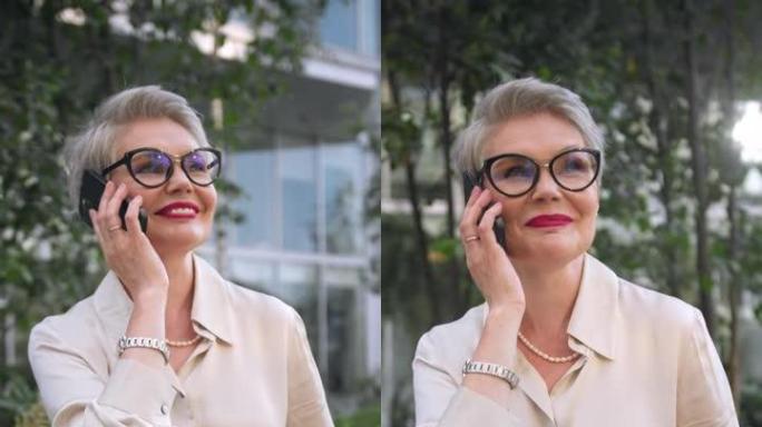 一位美丽的白发女商人面带微笑地在电话中愉快地交谈，而相机则将她从一侧拍摄到另一侧