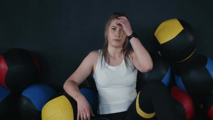 美丽的年轻高加索运动员女子坐在健身房地板上的健身球，锻炼后筋疲力尽。