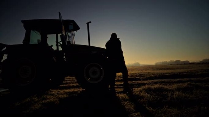 剪影农民在日落时分从农村的拖拉机上出来