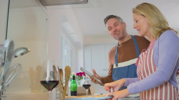 家里的成熟夫妇在一起准备饭菜时，在厨房的数字平板电脑上遵循食谱