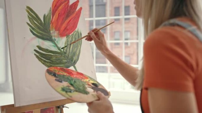 一位女画家在工作室的画布上绘画。女孩在后面的工作室里创作自然艺术品。创意艺术家独自在工作室创造一件美