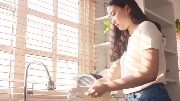 迷人的年轻亚洲女士一边洗碗，一边在家里的厨房打扫卫生。