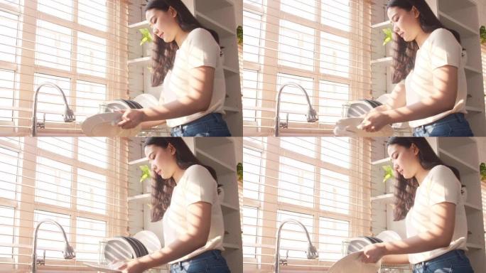 迷人的年轻亚洲女士一边洗碗，一边在家里的厨房打扫卫生。