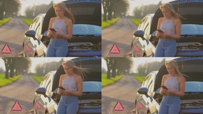 乡间小路上的危险警告标志，一名女子站在抛锚的汽车旁边，引擎盖朝上，用手机发短信寻求帮助-慢动作拍摄