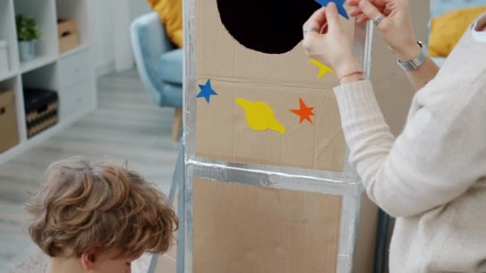 年轻女子和小儿子在家用太空设计贴纸装饰手工火箭