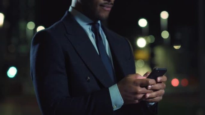 晚上在街上用智能手机关闭一个穿着西装的黑人的手。男性首席执行官保持联系，使用互联网与员工沟通并监控项