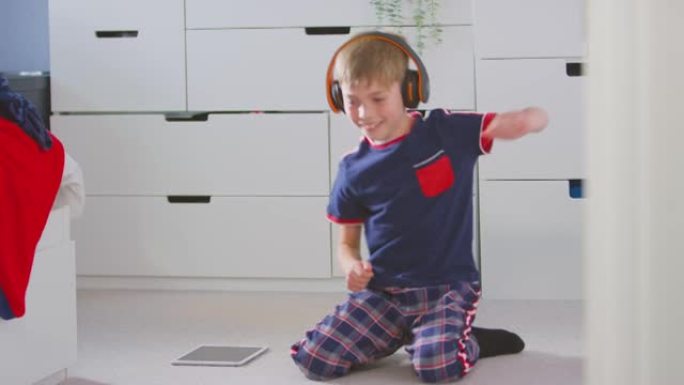 卧室里的男孩戴着无线耳机在数字平板电脑上听音乐
