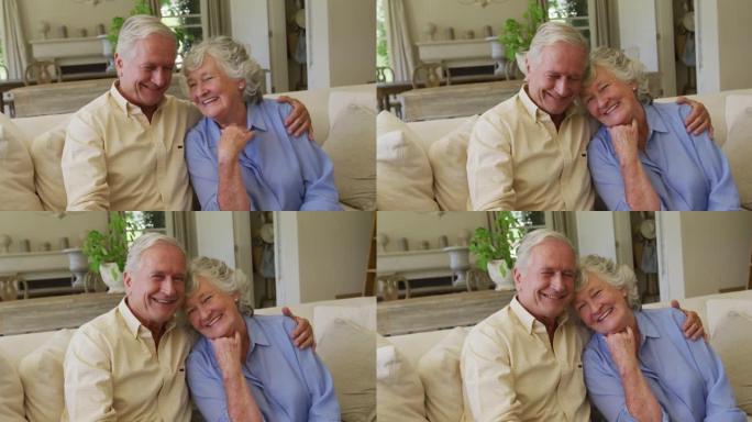 微笑的高加索高级夫妇坐在家里的沙发上互相拥抱的肖像