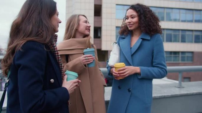 团结概念。在阴天，美丽的多民族年轻女性朋友在外面用生态杯子喝咖啡聊天。