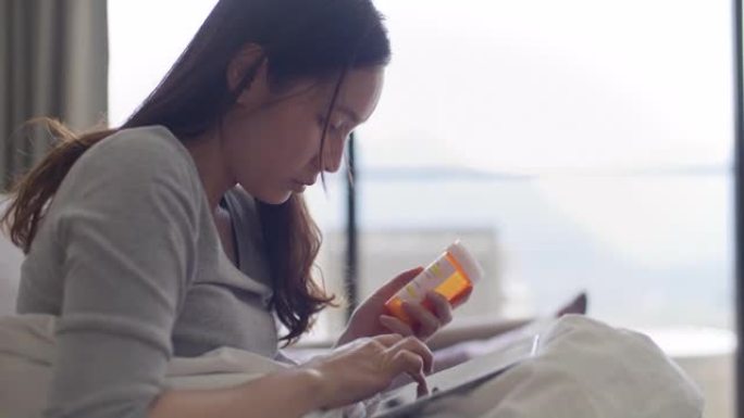 年轻的亚洲妇女拿着药瓶在家用手机聊天